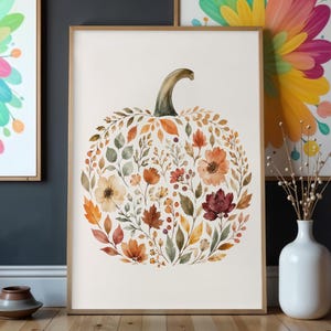 Puede incluir: Una impresión de arte mural rectangular que presenta una ilustración en acuarela con forma de calabaza compuesta por varios elementos botánicos de temática otoñal, incluyendo hojas, flores y bayas de color naranja, rojo y marrón sobre un fondo crema.