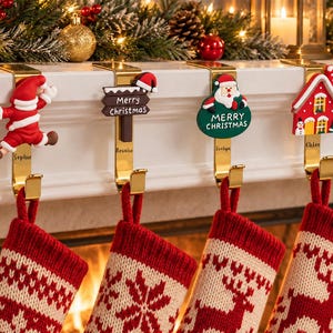 May include: Four gold-toned metal stocking holders with decorative Christmas-themed toppers including a Santa Claus, a sign reading Merry Christmas, a Santa in a green circle, and a house, each featuring a personalized name tag and red stockings.