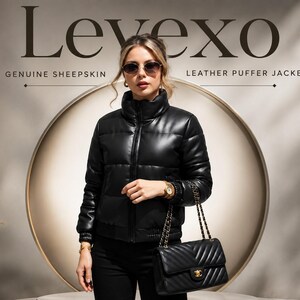 Puede incluir: Una chaqueta acolchada de piel de oveja negra con cuello alto y cierre de cremallera frontal. El texto Levexo Genuine Sheepskin Leather Puffer Jacket aparece en el fondo. La chaqueta presenta paneles acolchados horizontales y puños acanalados.