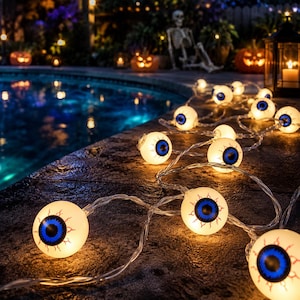 May include: A string of decorative lights featuring spherical bulbs designed to resemble eyeballs. Each white bulb has a bright blue iris, a black pupil, and red vein details. The lights are connected by a clear wire and emit a warm glow.