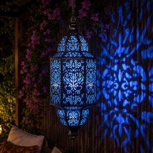 Peut inclure: Une lanterne suspendue avec un cadre en métal sombre et des motifs découpés complexes qui émettent une lumière bleue vive. La lanterne présente une forme allongée à multiples facettes avec des motifs filigranés symétriques.