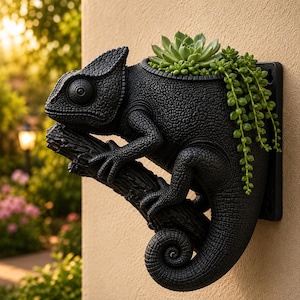 May include: A black wall-mounted planter shaped like a chameleon perched on a textured branch. The chameleon has a detailed, pebbled skin texture and a curled tail. A green succulent plant and a trailing string of pearls plant grow from the top.