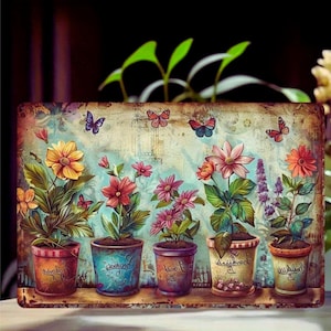May include: A rectangular metal sign featuring a vintage-style illustration of five potted plants with colourful flowers, including yellow, red, and pink blossoms. Several butterflies are depicted flying above the pots against a textured background.
