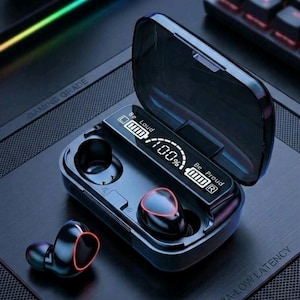 May include: A pair of black wireless earbuds with red circular accents and a charging case featuring a digital display screen. The screen shows the text Be Loud and Be Proud with a 100% battery indicator. One earbud is inside the case, and one is outside.