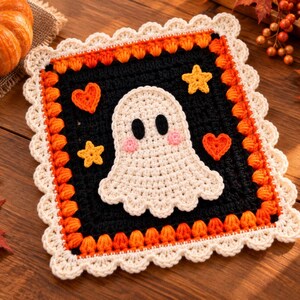 Peut inclure: Un dessous de plat carré au crochet représentant un fantôme blanc central avec des yeux noirs et des joues roses sur fond noir. Le motif inclut des cœurs orange et des étoiles jaunes, bordé d'une frise orange et d'un contour festonné crème.