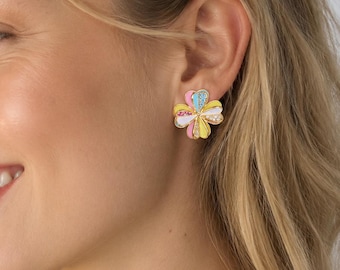 Könnte beinhalten: Ein Ohrstecker in Form einer vierblättrigen Blume. Jedes Blütenblatt ist in einer anderen Pastellfarbe emailliert, darunter Hellblau, Gelb, Rosa und Weiß. Die Mitte der Blume ist mit kleinen, klaren, funkelnden Steinen verziert.