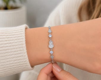 Könnte beinhalten: Ein silberfarbenes Kettenarmband mit einem zentralen kürbisförmigen weißen Steinelement, flankiert von kleinen runden klaren Steinen und zarten Pavé-Akzenten. Das Armband ist mit einer dünnen Metallgliederkette und einem Verschluss gefertigt.