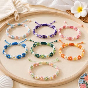 May include: Seven handmade bracelets featuring small crocheted flower motifs in various color combinations, including blue, purple, pink, green, orange, and yellow, each with adjustable cord closures arranged on a circular wooden tray.