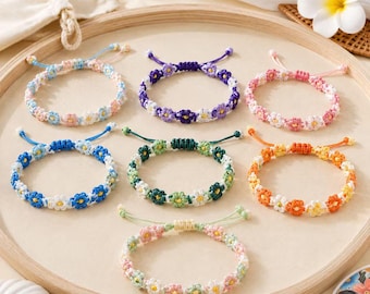 May include: Seven handmade bracelets featuring small crocheted flower motifs in various color combinations, including blue, purple, pink, green, orange, and yellow, each with adjustable cord closures arranged on a circular wooden tray.