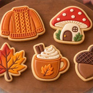 Può includere: Cinque biscotti decorati a forma di maglione a trecce, casa a fungo, foglia d'acero, tazza di cioccolata calda con bastoncini di cannella e ghianda. I biscotti presentano dettagli in glassa arancione, rossa, marrone e bianca.