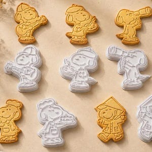 Può includere: Una collezione di quattro biscotti dorati e quattro stampini per biscotti in plastica bianca abbinati. Ogni articolo raffigura un personaggio cane dei cartoni animati in vari ruoli, tra cui suonare la chitarra, dipingere, usare un telescopio, preparare una torta e indossare un cappello.