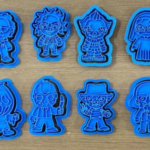 Könnte beinhalten: Ein Set aus acht hellblauen Kunststoff-Ausstechformen, die stilisierte Cartoon-Versionen verschiedener Horrorfilm-Charaktere zeigen, darunter Figuren mit Masken, Hüten und markanten Outfits, angeordnet in zwei Reihen zu je vier Stück.