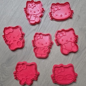 Pode incluir: Um conjunto de seis cortadores de biscoito de plástico vermelho brilhante, cada um apresentando o rosto ou a silhueta completa da personagem Hello Kitty. A coleção inclui várias poses, como segurar uma flor, um coração e usar óculos.