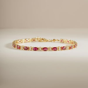 May include: A gold chain bracelet featuring a repeating pattern of oval-cut deep pink rubies alternating with small, clear, round-cut white stones. The bracelet is constructed with a delicate metal link design and includes a secure clasp mechanism.