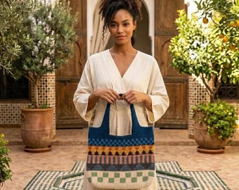 Puede incluir: Un bolso tote rectangular de ganchillo con un patrón geométrico en tonos azul oscuro, naranja, amarillo, gris y crema. El bolso tiene dos asas integradas y una base estructurada, mostrando un diseño de tapiz multicolor en toda la pieza.