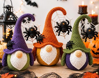 Puede incluir: Tres gnomos de ganchillo con sombreros altos y curvos en morado, naranja y verde. Cada gnomo tiene una barba blanca, una nariz redonda y una telaraña de ganchillo blanca unida a la punta del sombrero, con una araña negra sobre ella.