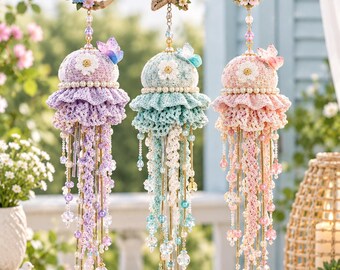 Puede incluir: Tres adornos colgantes de medusas en color lavanda, verde menta y rosa suave. Cada uno presenta una cúpula de ganchillo, una falda con volantes y largos tentáculos de cuentas. Están suspendidos de una luna creciente, una estrella y un corazón.