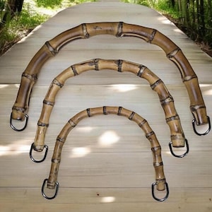 Puede incluir: Tres asas de bambú natural con anillos metálicos. Las asas son de diferentes tamaños y están dispuestas en semicírculo.