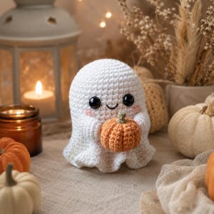 Puede incluir: Una figura de fantasma tejida a ganchillo en color blanco con ojos de seguridad negros, una peque&ntilde;a sonrisa bordada y mejillas sonrosadas. El fantasma sostiene entre sus brazos una peque&ntilde;a calabaza de ganchillo naranja con tallo verde.