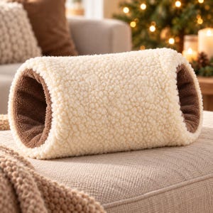 Könnte beinhalten: Ein zylindrischer Handwärmer mit einer strukturierten, cremefarbenen Sherpa-Fleece-Außenseite und einem weichen, braunen Fleece-Innenfutter. Das röhrenförmige Accessoire hat offene Enden, die den Kontrast zwischen der hellen Außenschicht und dem dunklen Stoff zeigen.