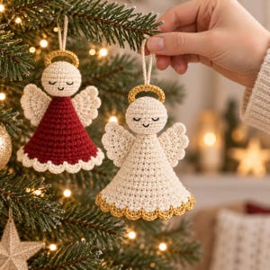 May include: Two crocheted angel ornaments hanging from a Christmas tree. One angel features a deep red dress with a cream-colored scalloped hem, while the other is entirely cream-colored with a gold scalloped hem. Both have gold halos.