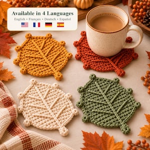 Puede incluir: Cuatro posavasos de ganchillo con forma de hoja en amarillo mostaza, naranja quemado, crema y verde salvia. Una taza de cerámica descansa sobre el posavasos naranja. Un cartel arriba dice Available in 4 Languages con texto en varios idiomas.