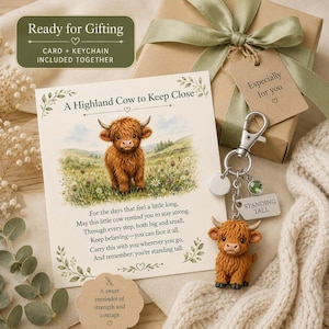 Könnte beinhalten: Ein Geschenkset bestehend aus einer quadratischen Karte mit einer Highland-Rind-Illustration und dem Text A Highland Cow to Keep Close sowie einem Metall-Schlüsselanhänger mit einer Highland-Rind-Figur und einem Schild mit der Aufschrift STANDING TALL.