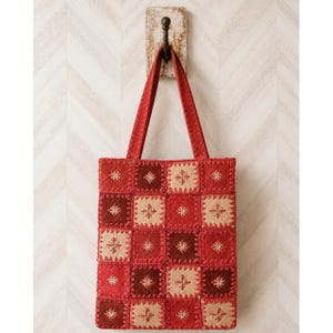 May include: A rectangular tote bag constructed from a grid of square patches in shades of red, dark red, and beige. Each square features a central embroidered star-like motif and is joined by visible decorative stitching along the edges.