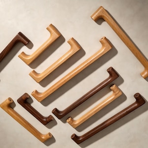 Peut inclure: Une collection de poign&eacute;es de placard en bois de diff&eacute;rentes longueurs et teintes, allant du ch&ecirc;ne clair au noyer fonc&eacute;. Chaque poign&eacute;e pr&eacute;sente un design lisse et incurv&eacute; avec deux points de fixation aux extr&eacute;mit&eacute;s, dispos&eacute;es en vrac.