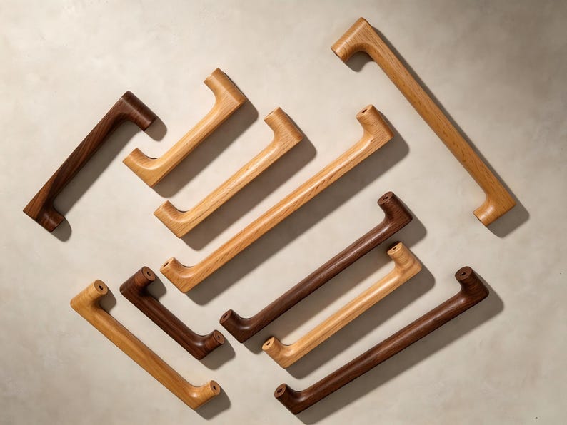 Peut inclure: Une collection de poign&eacute;es de placard en bois de diff&eacute;rentes longueurs et teintes, allant du ch&ecirc;ne clair au noyer fonc&eacute;. Chaque poign&eacute;e pr&eacute;sente un design lisse et incurv&eacute; avec deux points de fixation aux extr&eacute;mit&eacute;s, dispos&eacute;es en vrac.