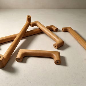 Peut inclure: Un ensemble de quatre poign&eacute;es de placard en bois brun clair au design cylindrique et lisse. Chaque poign&eacute;e pr&eacute;sente deux points de fixation circulaires aux extr&eacute;mit&eacute;s, avec des trous de vis m&eacute;talliques visibles au centre des faces plates.