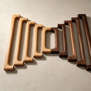 Peut inclure: Une collection de neuf poign&eacute;es de placard en bois dispos&eacute;es en d&eacute;grad&eacute;, du ch&ecirc;ne clair au noyer fonc&eacute;. Les poign&eacute;es pr&eacute;sentent un design rectangulaire allong&eacute; avec des bords arrondis et un grain de bois visible, variant en longueur.