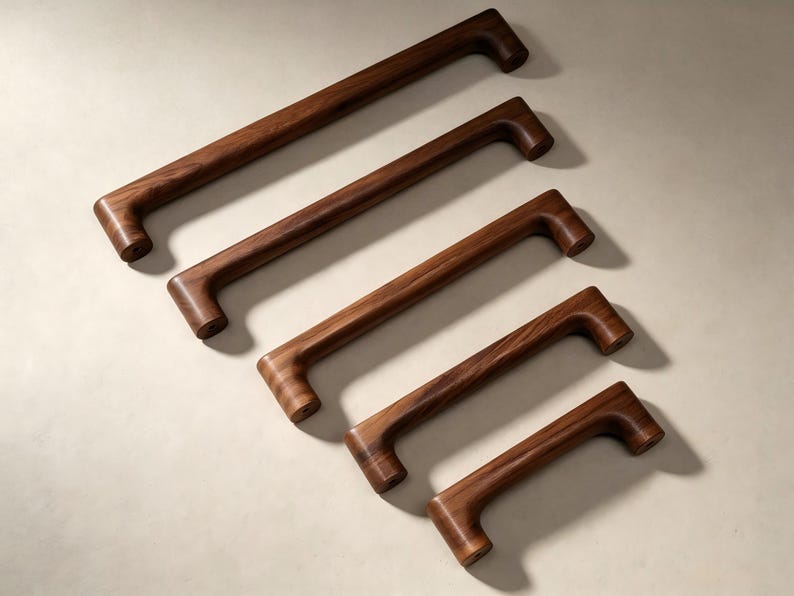 Peut inclure: Cinq poign&eacute;es de placard en bois brun fonc&eacute; dispos&eacute;es en diagonale, de la plus longue &agrave; la plus courte. Chaque poign&eacute;e pr&eacute;sente un design en barre rectangulaire lisse avec des bords arrondis et des points de fixation cylindriques aux extr&eacute;mit&eacute;s.