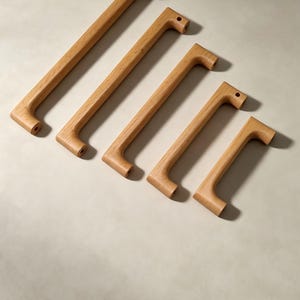 Peut inclure: Cinq poign&eacute;es de placard en bois brun clair dispos&eacute;es en diagonale, de la plus longue &agrave; la plus courte. Chaque poign&eacute;e pr&eacute;sente une finition lisse en grain de bois naturel, une forme de barre rectangulaire et deux trous de montage circulaires.