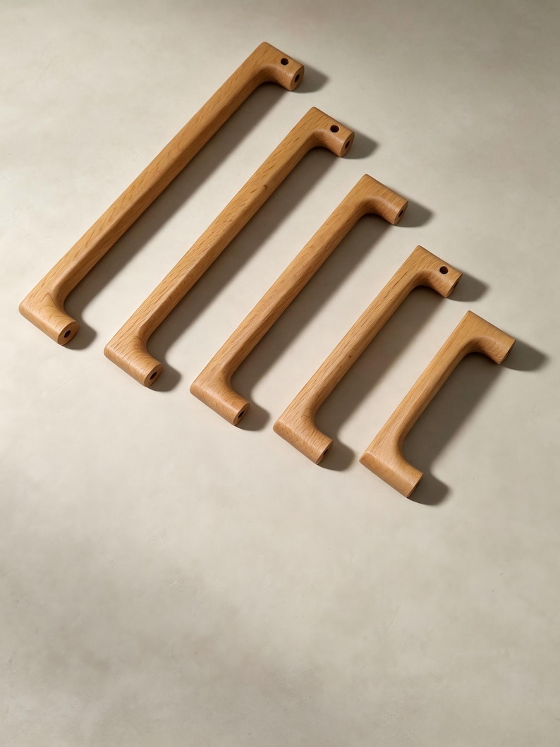 Peut inclure: Cinq poign&eacute;es de placard en bois brun clair dispos&eacute;es en diagonale, de la plus longue &agrave; la plus courte. Chaque poign&eacute;e pr&eacute;sente une finition lisse en grain de bois naturel, une forme de barre rectangulaire et deux trous de montage circulaires.