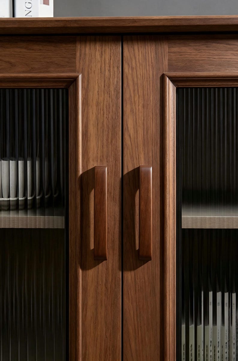 Peut inclure: Une armoire en bois brun fonc&eacute; dot&eacute;e de deux portes avec des panneaux en verre cannel&eacute; vertical. Chaque porte poss&egrave;de une poign&eacute;e en bois massif assortie. &Agrave; l'int&eacute;rieur, des &eacute;tag&egrave;res claires contiennent des rang&eacute;es de livres blancs.