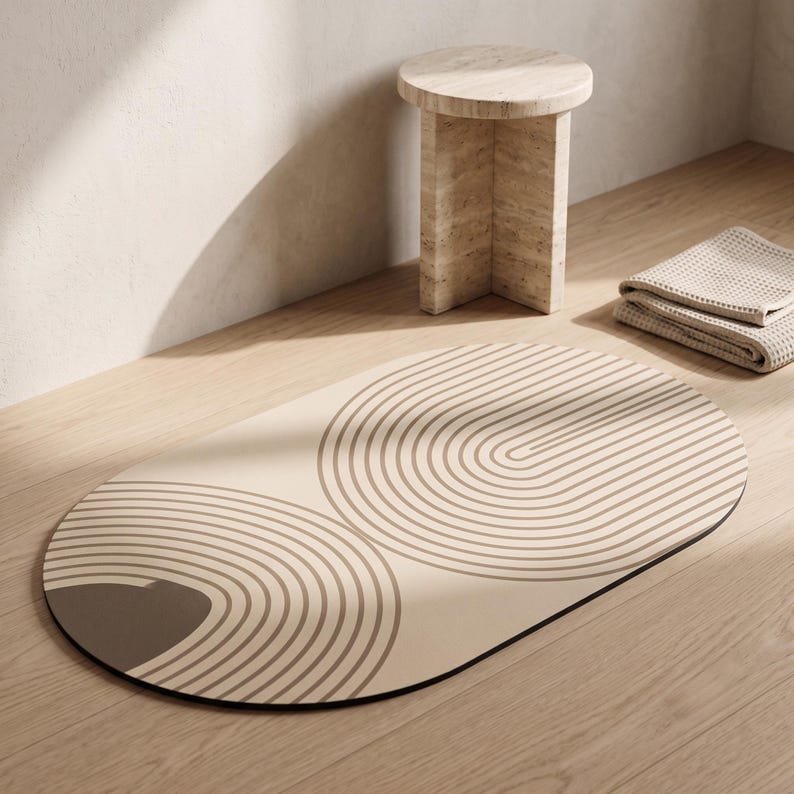 May include: An oval-shaped floor mat featuring a beige base color with dark brown concentric arch patterns. The mat has a smooth surface and a dark edge trim, displaying a repeating geometric design of curved lines across its entire length.