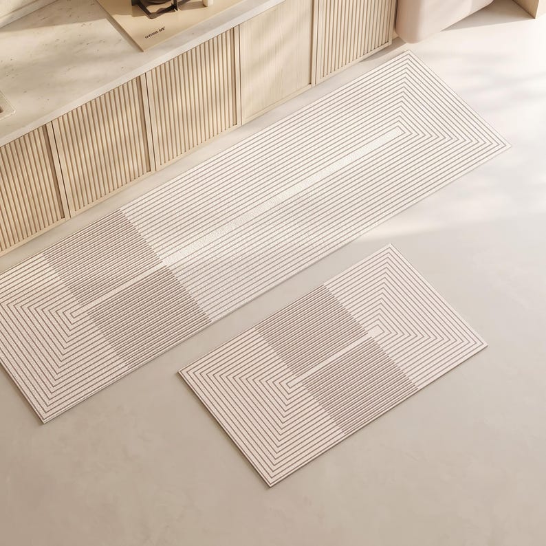 May include: A set of two rectangular floor mats featuring a cream-colored base with a repeating pattern of thin, dark brown concentric lines that form geometric shapes across the surface, creating a linear and structured visual design.