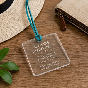 May include: A clear square acrylic luggage tag with a teal cord. The tag features white printed text: CHLOE MARTINEZ, a heart icon, 812 Apricot Lane, Austin, TX 78701, +1 512 555 0198, Adventure Awaits, and the date Since 07.21.2024.