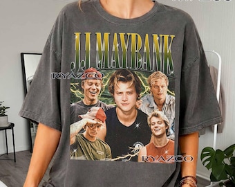 Puede incluir: Una camiseta de manga corta gris carbón con un estampado gráfico de J.J. Maybank. El diseño incluye el texto "J.J. MAYBANK" en una fuente con degradado amarillo y verde sobre un collage de cuatro imágenes del personaje con detalles de rayos.