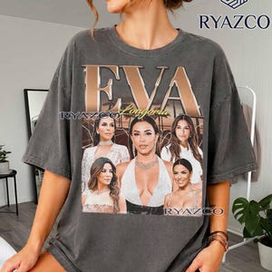 May include: A charcoal gray oversized t-shirt featuring the text EVA Longoria in large metallic gold and script lettering. The graphic includes five distinct photographic portraits of Eva Longoria arranged in a collage format on the front.