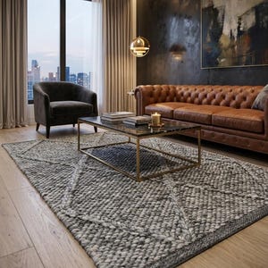 May include: A rectangular area rug featuring a chunky, hand-knitted texture in shades of charcoal and light grey. The rug displays a prominent geometric diamond pattern woven into the thick, heavy yarn, covering the floor in a living room space.