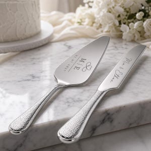 May include: A silver cake server and knife set with hammered metal handles. The server features the engraved text M | E, a heart symbol, and the date 07.07.2027. The knife is engraved with the names Mia & Ethan in a cursive script font.