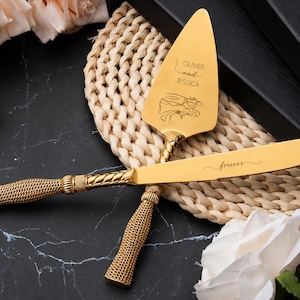 Puede incluir: Un juego de cuchillo y pala para pastel en tono dorado con mangos texturizados estilo cuerda. La pala está grabada con el texto OLIVER and JESSICA sobre un dibujo lineal de dos manos, mientras que la hoja del cuchillo tiene la palabra forever.