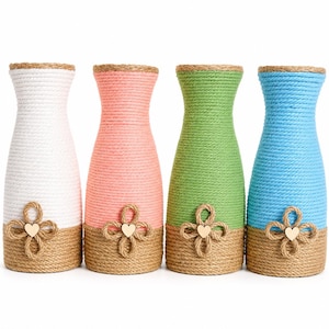 May include: Four cylindrical vases wrapped in coloured rope, featuring white, pink, green, and blue upper sections with natural tan rope bases. Each vase is decorated with a four-loop rope flower accent centred with a small wooden heart.