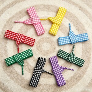 May include: Eight rolls of fabric ribbon arranged in a circle, each featuring a white and colored gingham check pattern. The colors include pink, yellow, light blue, red, dark green, purple, black, and a second shade of green.