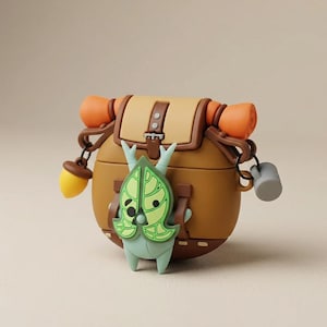 May include: A brown silicone protective case for wireless earbuds designed to look like a hiking backpack. It features a tan flap, orange rolled sleeping bag, a yellow acorn charm, a grey mug charm, and a light green leaf-shaped creature figure.