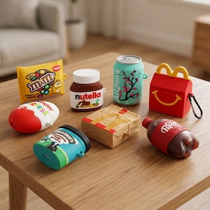 Op de afbeelding: Een verzameling siliconen beschermhoesjes voor draadloze oordopjes, met ontwerpen geïnspireerd op M&M's, Nutella, Arizona-thee, een McDonald's Happy Meal-doos, Kinder Surprise, Ben & Jerry's ijs, een papieren zak en een Dr. Pepper-flesje.