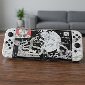 Può includere: Una console portatile bianca con una skin grafica in bianco e nero raffigurante un angelo in stile anime, un serpente scheletrico e il testo "Did you see the drool I sent you?" e "whisper.. whisper.." sulla parte anteriore e sui controller.