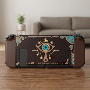 Peut inclure: Une console Nintendo Switch marron foncé arborant un motif d'œil stylisé au centre avec des accents bleu clair et jaunes. L'arrière de l'appareil présente des lignes complexes beige et bleu ainsi que le texte NINTENDO SWITCH en bas.